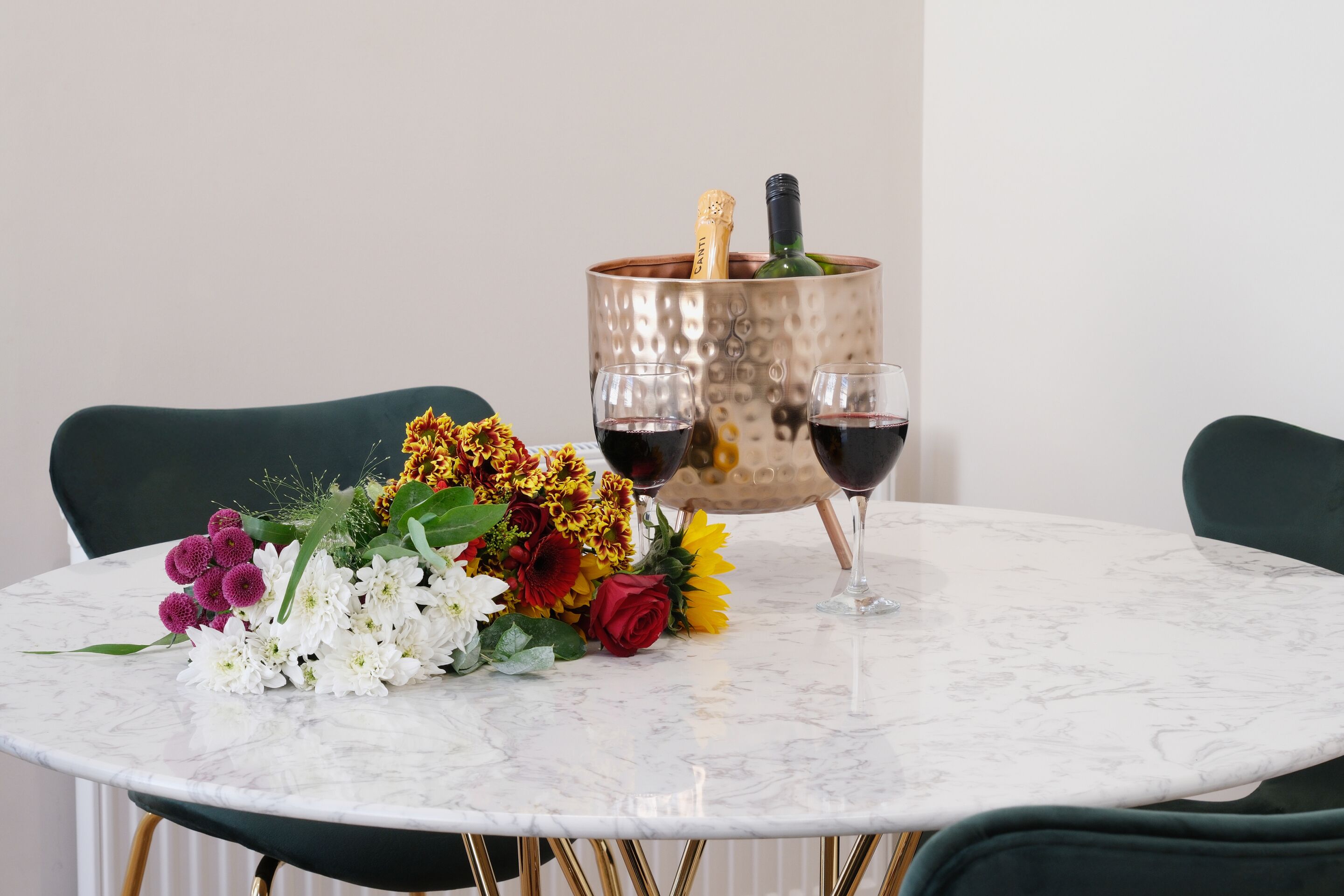 Ein runder Marmortisch mit einem Blumenstrauß, zwei Weingläsern und einer Champagnerflasche in einem Kupfergefäß.