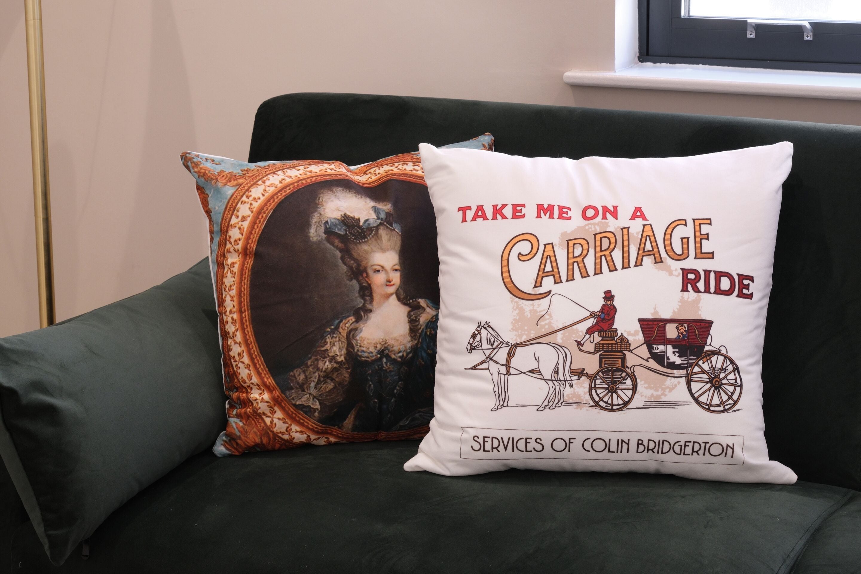 A green sofa with two decorative pillows, one with a carriage ride illustration and text, and the other with a vintage portrait.