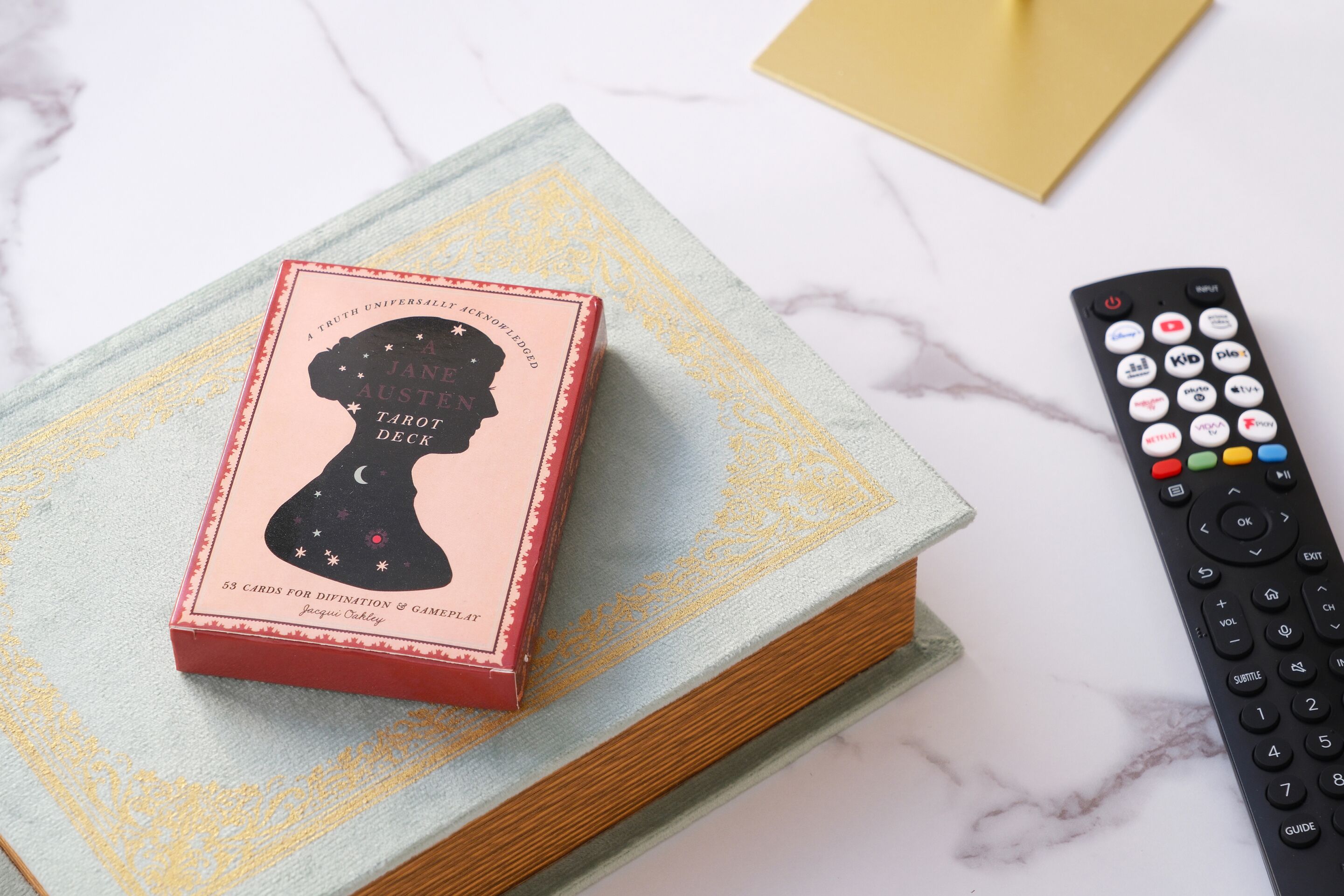 A tarot deck box on a book with a remote control beside it.