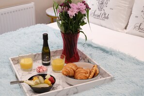 A breakfast tray with croissants, fruit, juice, and a bottle of wine on a fluffy blue blanket. - Dream Stays Bath - John Street  (Bath)