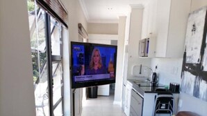 Ein modernes Wohnzimmer mit einem braunen Ledersofa, einem an der Wand montierten Fernseher und einer Küche im Hintergrund.