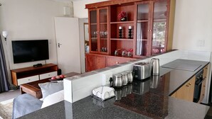 A modern kitchen with a central island, built-in cabinets, a flat-screen TV, and a dining area with a sofa and table. - SkyView, a spacious modern cottage. (Johannesburg)