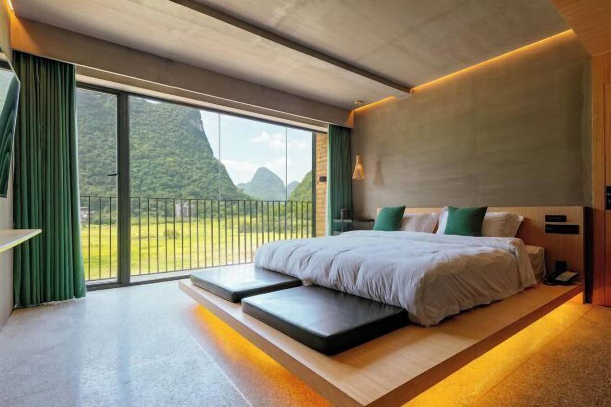 A modern bedroom with a large bed, a view of greenery, and a balcony.