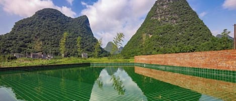 Une piscine dont le fond est recouvert de carreaux, ce qui crée un effet de miroir reflétant le paysage environnant, notamment une montagne et un mur de briques.