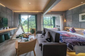Ein modernes Hotelzimmer mit einem großen Bett, einer Couch, einem Esstisch mit einer Tischdecke und Blick auf die Berge.