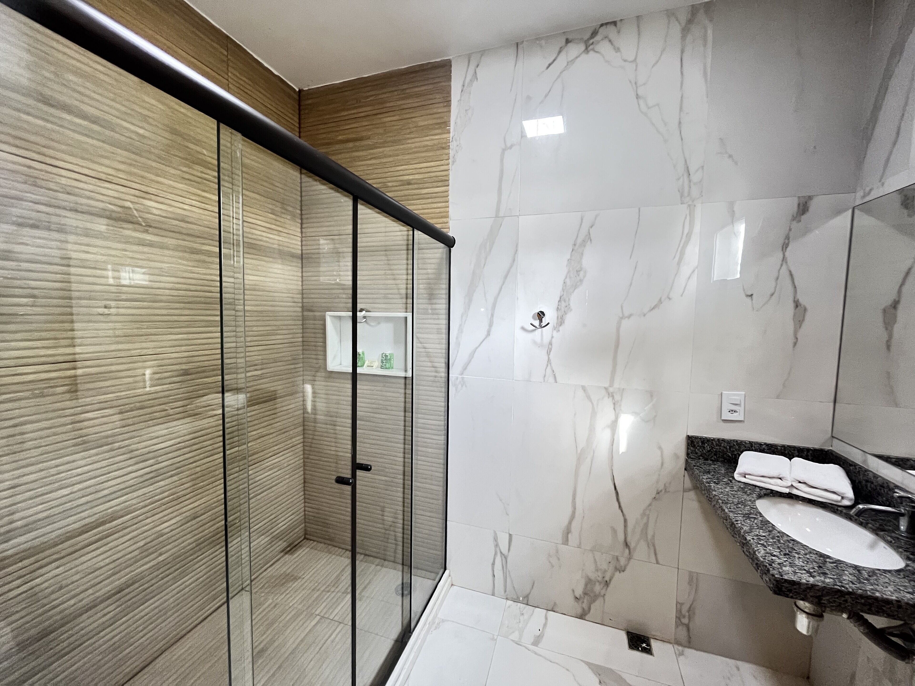 Ein modernes Badezimmer mit einer gläsernen Dusche, einer Marmorwand und einer Arbeitsplatte aus Granit mit Waschbecken und Handtuchhalter.