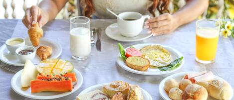 Mesa posta com itens de café da manhã, incluindo croissants, frutas, pão e doces.