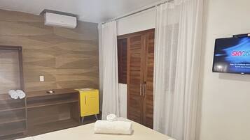 Una habitación de hotel con una cama grande, un armario de madera, un mueble amarillo y un televisor en la pared.
