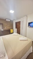 Una habitación de hotel con una cama grande, un armario de madera, un mueble amarillo y un televisor en la pared.