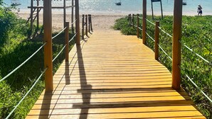 Una passera de fusta que condueix a una platja, amb una estructura de pergola.