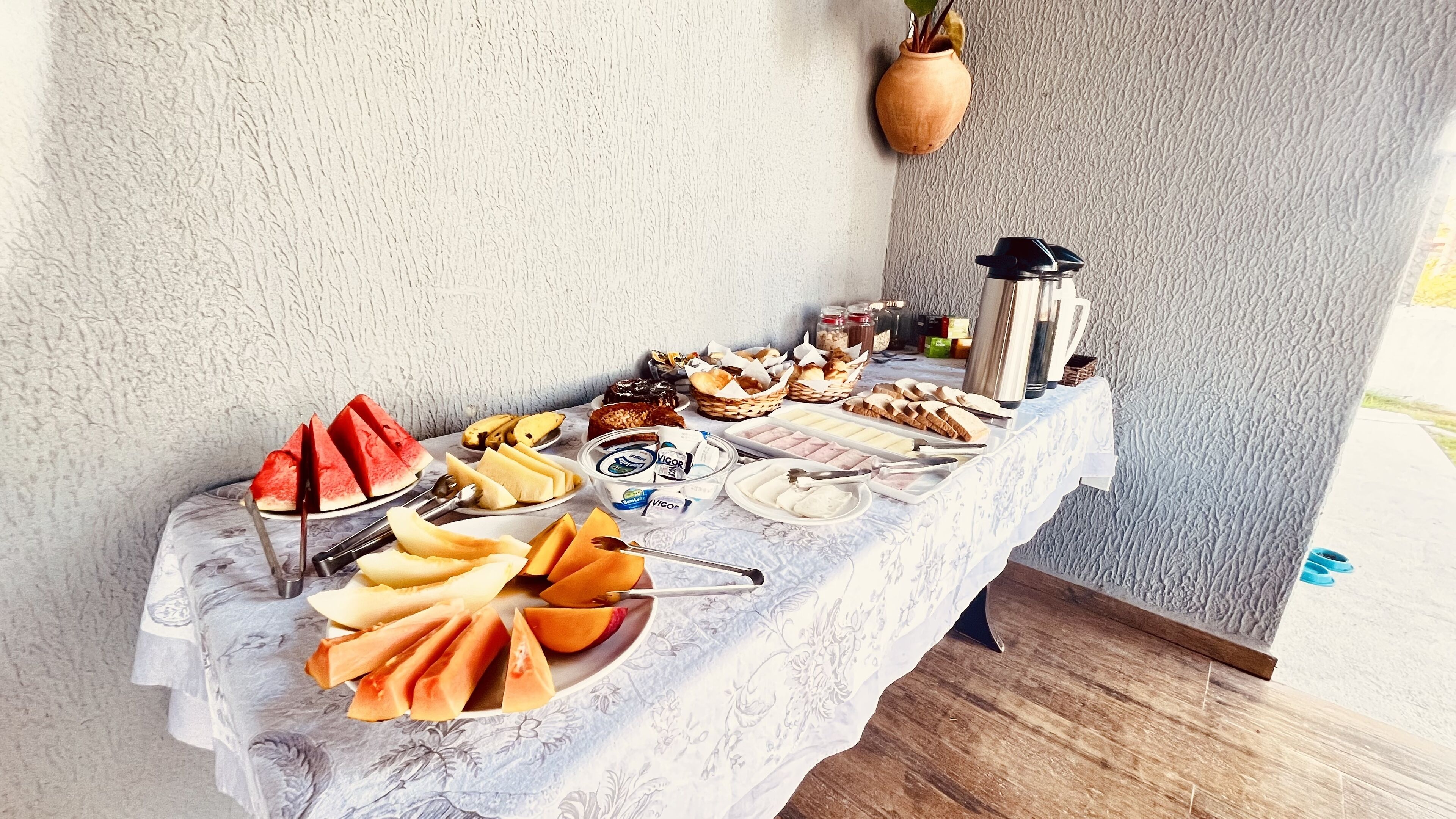 A table with various food items, including fruits, pastries, and condiments, set against a textured wall.