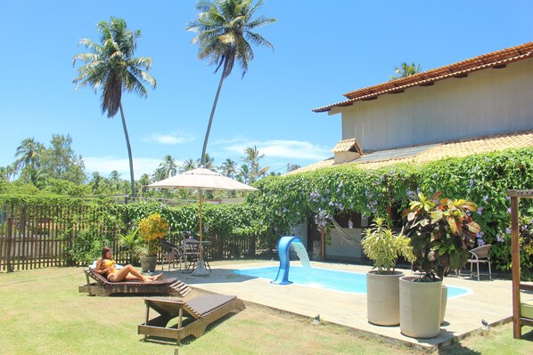 A backyard with a swimming pool, lounge chairs, and potted plants.
