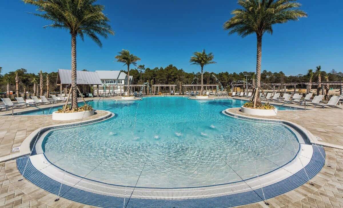 Uma piscina grande e convidativa com espreguiçadeiras e palmeiras, rodeada por um deck revestido de azulejos.