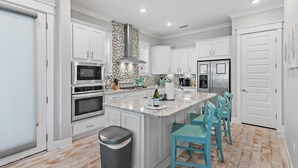A modern kitchen with white cabinets, stainless steel appliances, a granite countertop, and teal chairs. - New Golf Cart | Resort Style Pool | 3 Bikes | 30A (Panama City Beach)