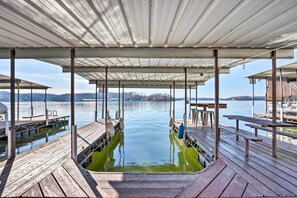 A wooden dock with a covered seating area overlooking calm water. - Lakefront Ozarks Home: Deck + Boat Dock! (Linn Creek)