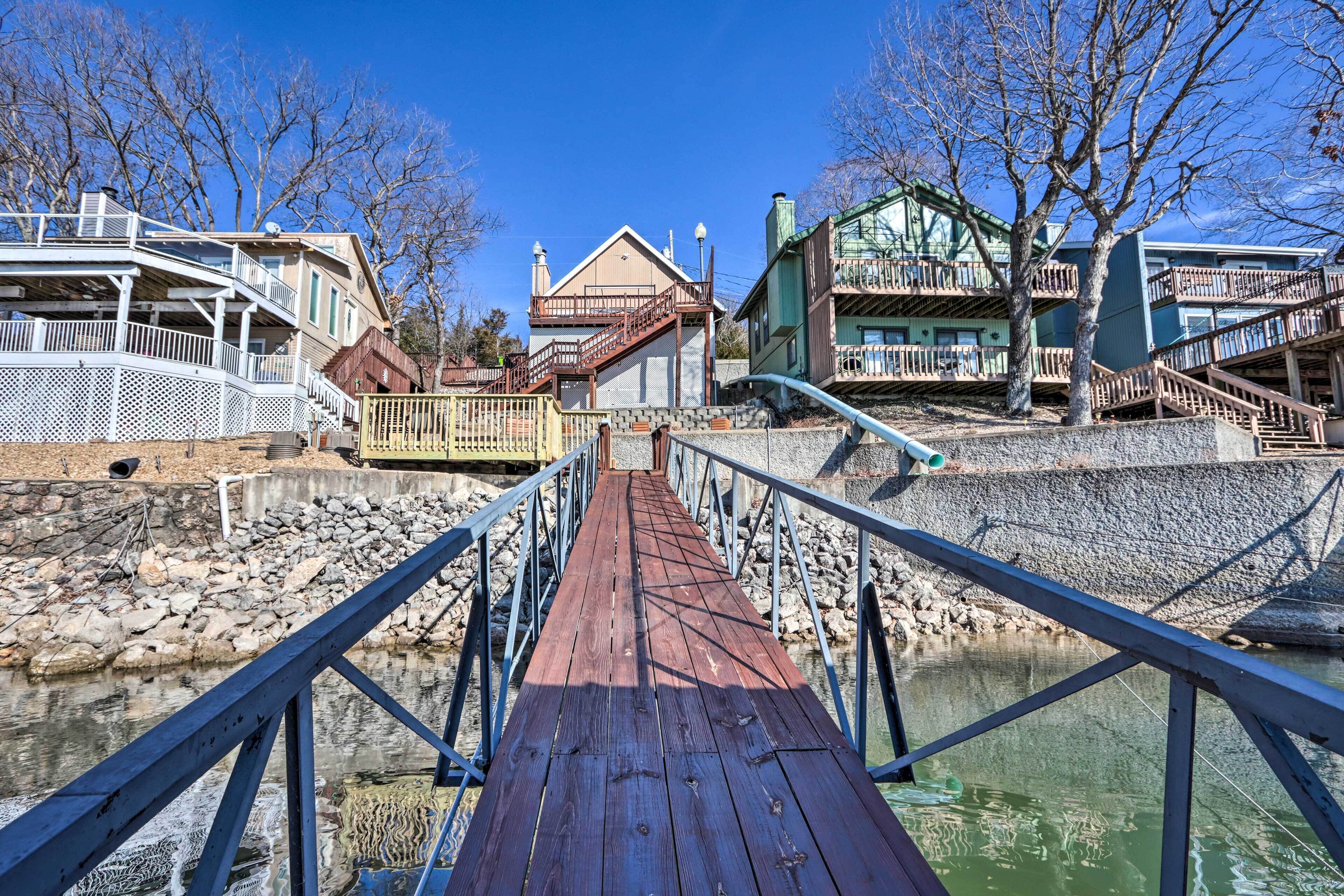 A wooden bridge with railings leading to a building with multiple balconies and a green roof.