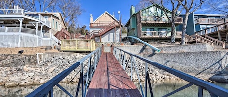 A wooden bridge with railings leading to a building with multiple balconies and a green roof.