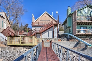 A wooden bridge leading to a building with a sloped roof and a staircase. - Lakefront Ozarks Home: Deck + Boat Dock! (Linn Creek)