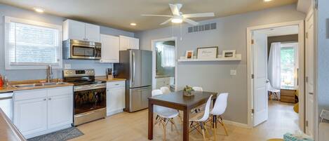 A modern kitchen with white cabinetry, stainless steel appliances, and a dining area with a wooden table and white chairs.