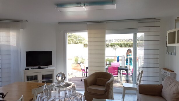 A living room with a TV, a coffee table, and a sofa. There is a sliding glass door leading to an outdoor area with a table and chairs. - LILLEAU DES NIGES, Residences Re holiday rentals villa Re (Saint-Clément-des-Baleines)