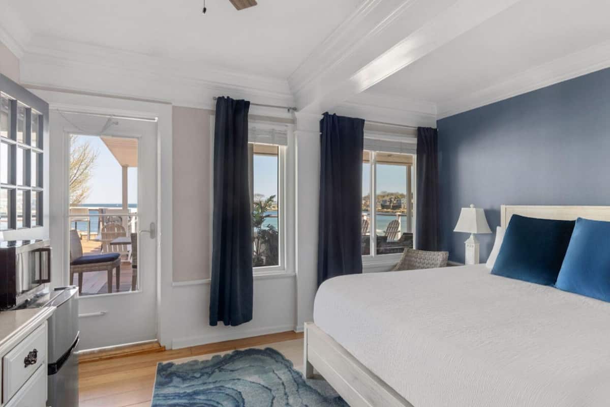 A bedroom with a large bed, a nightstand, a lamp, and a view of the outdoors.
