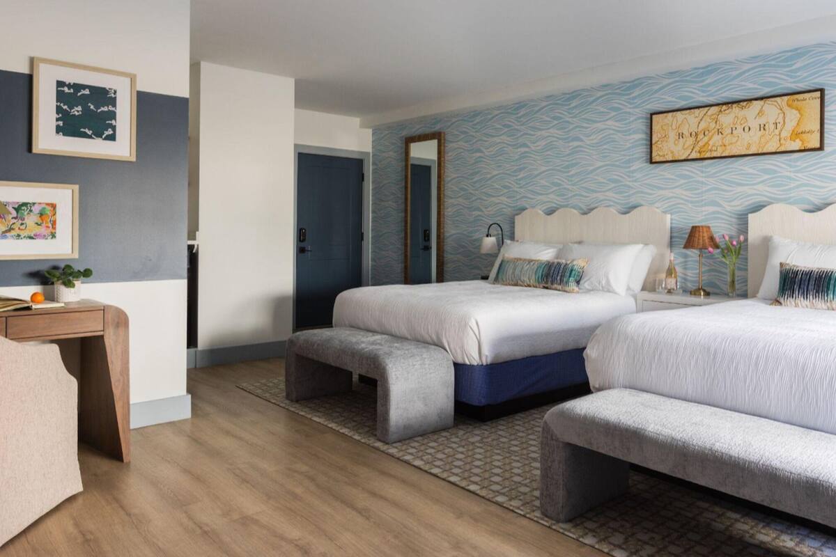 A hotel room with two beds, a desk, a chair, and a large map on the wall.