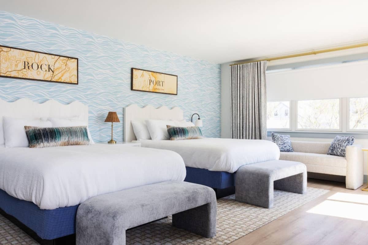 A hotel room with two beds, a sofa, a rug, and two wall-mounted artworks.