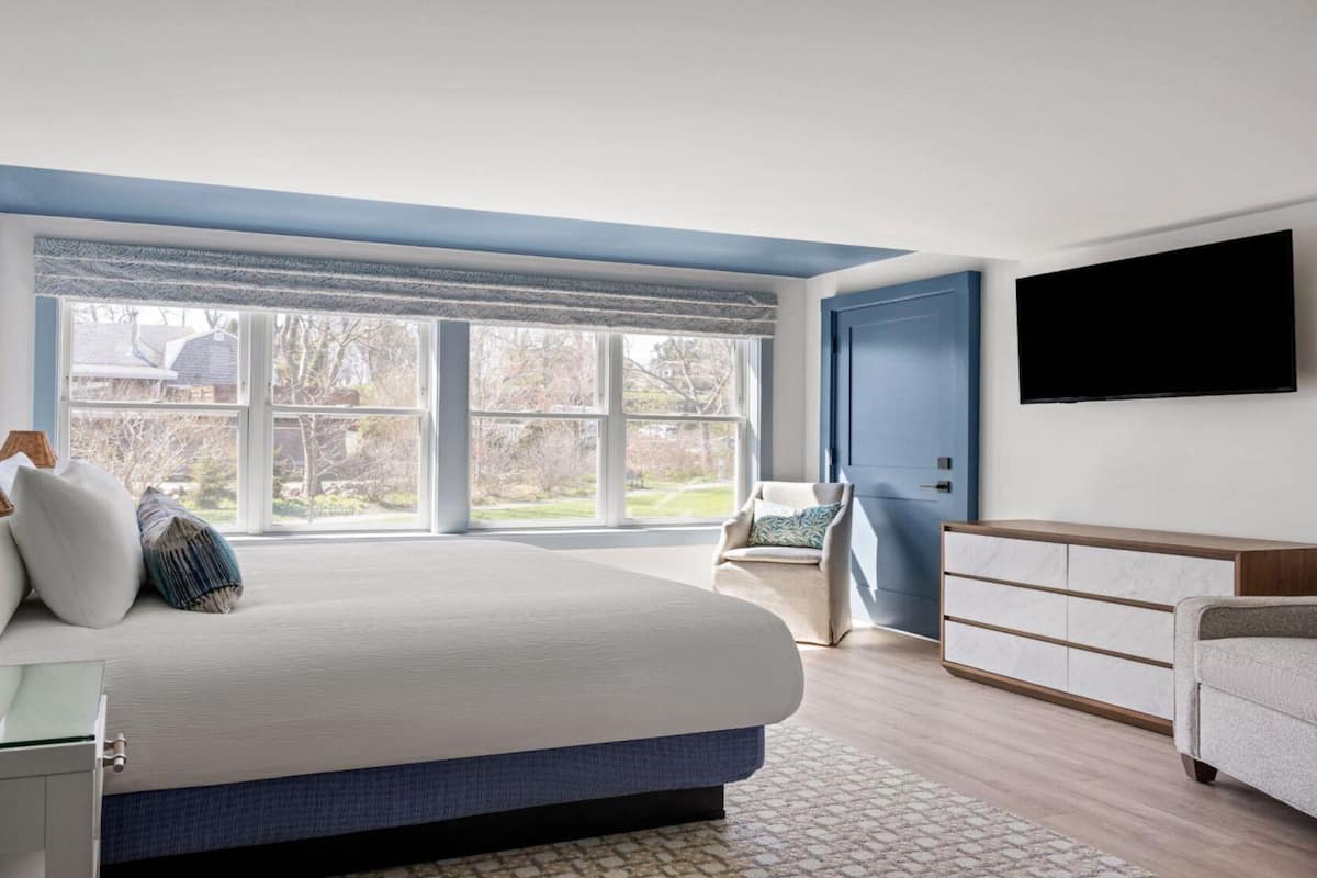 A bedroom with a large bed, a TV, a dresser, and a window with a view of the outdoors.