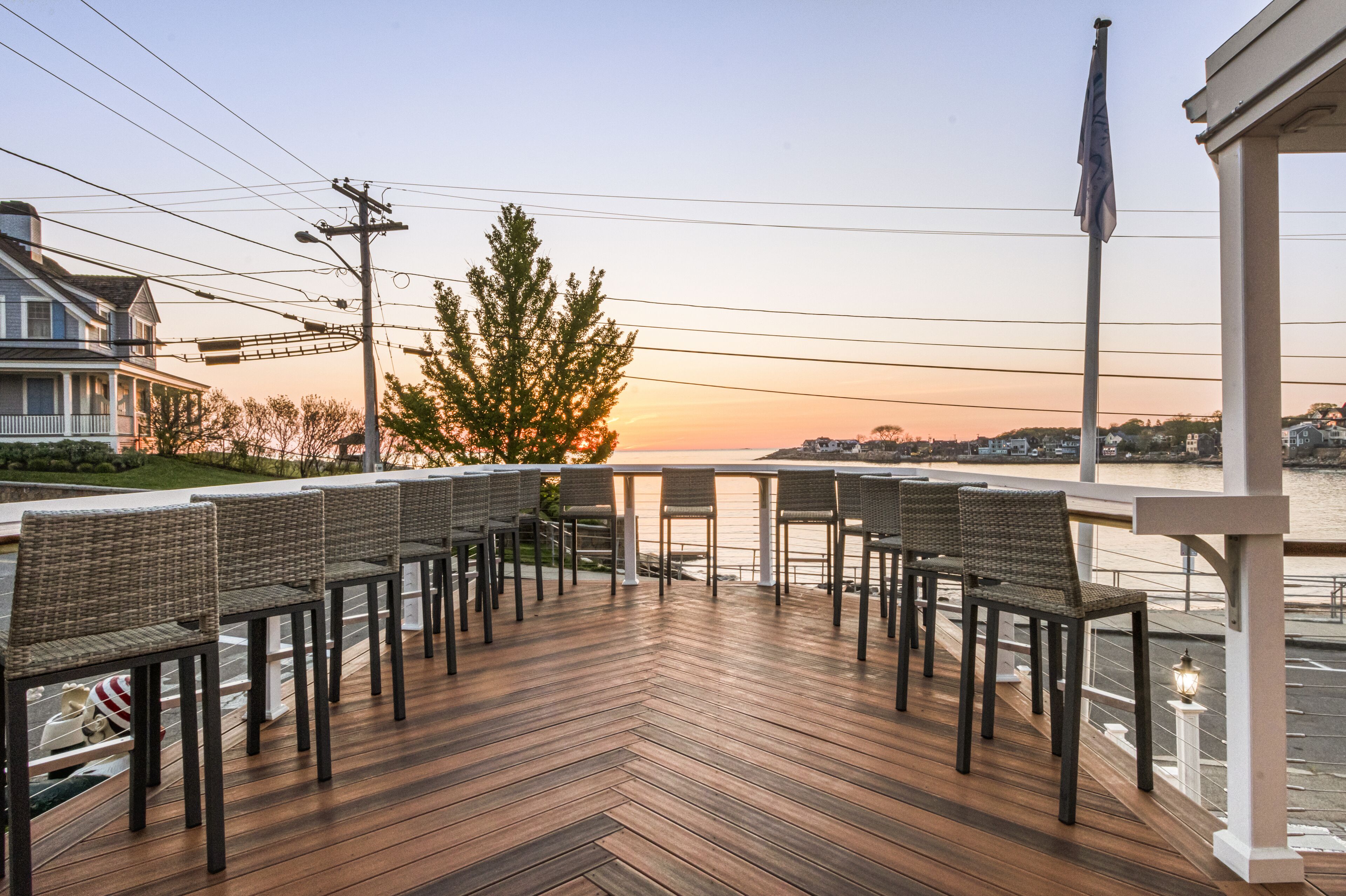 Terraza de madera con sillas de mimbre y barandilla con vista al agua.