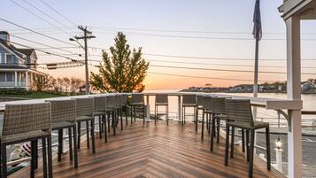 Terraza de madera con sillas de mimbre y barandilla con vista al agua.