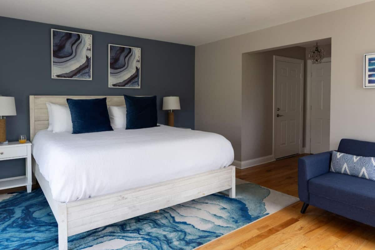 A bedroom with a bed, two bedside tables, a nightstand, a blue sofa, and artwork on the walls.