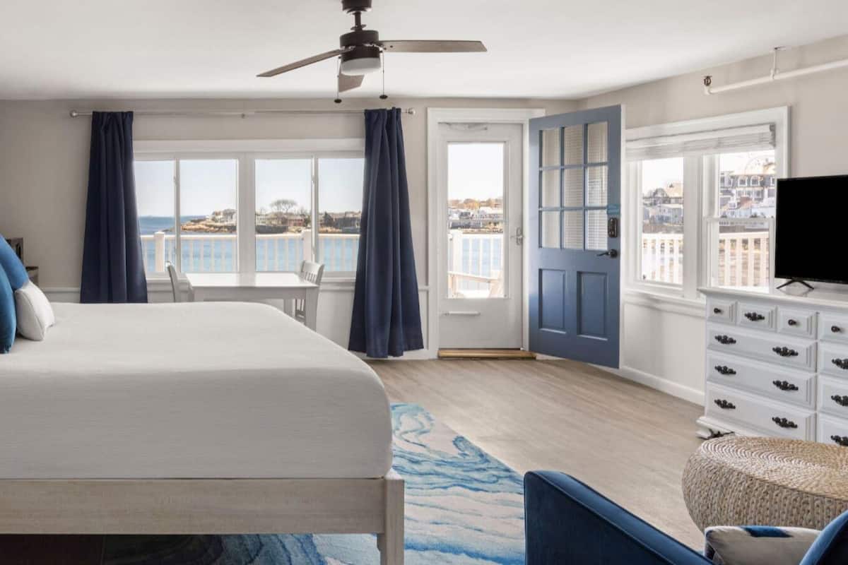 A bedroom with a bed, a ceiling fan, a view of the sea, a dresser, and a television.