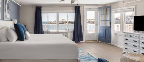 A bedroom with a bed, a ceiling fan, a view of the sea, a dresser, and a television.