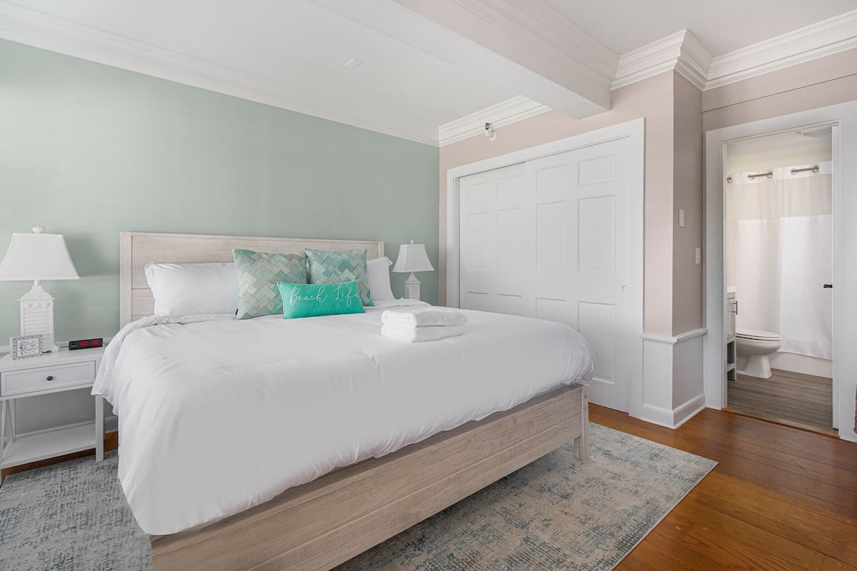 A bedroom with a bed, nightstands, a white door, and a bathroom visible through an open door.