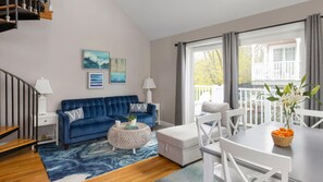 Ein modernes Wohnzimmer mit einem blauen Sofa, einem runden Couchtisch und einem Essbereich mit weißem Tisch und Stühlen.