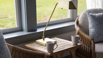 A cozy room with a wooden table, two white mugs, a lamp, and a view of greenery through a window.