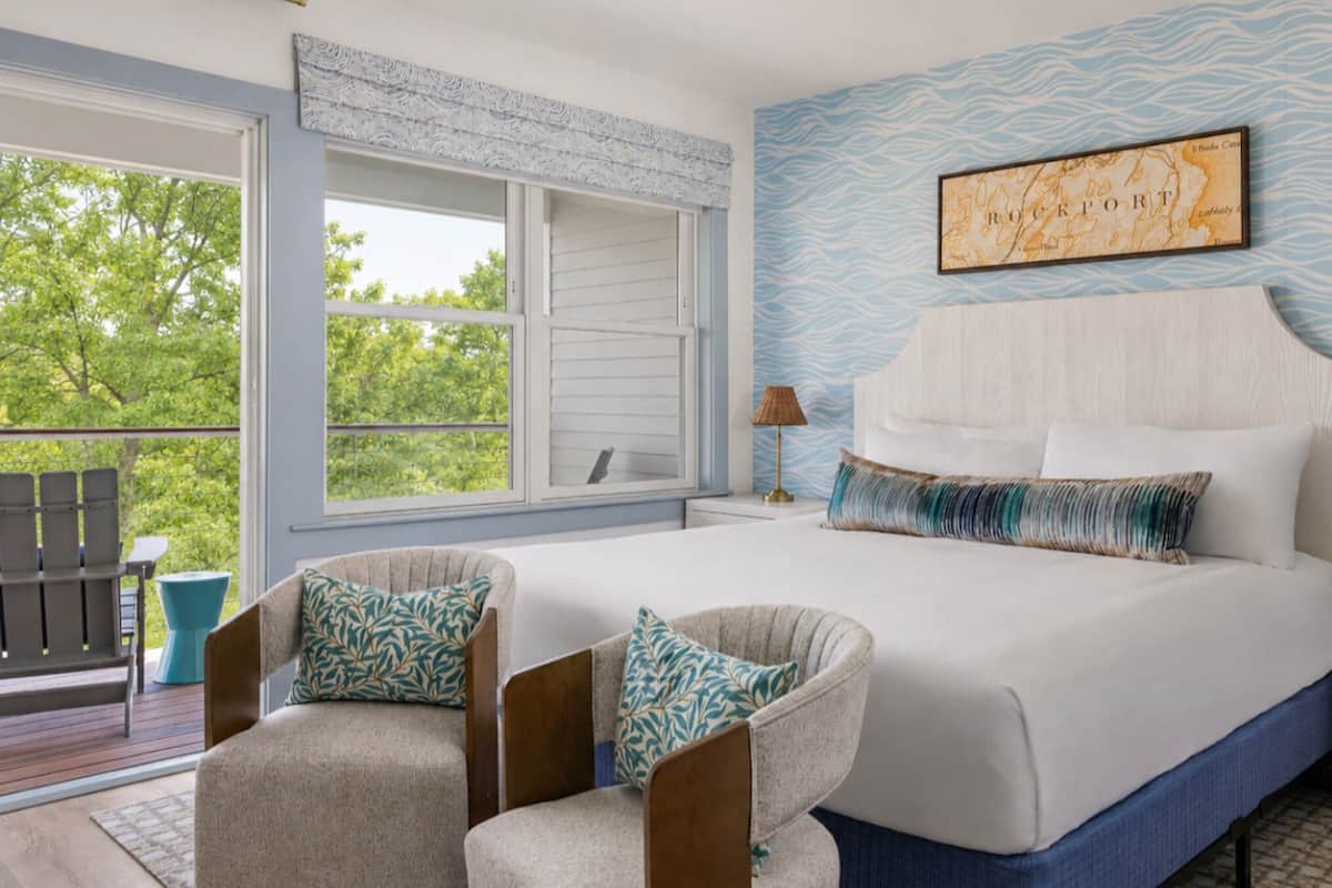 A bedroom with a large bed, two chairs, a window, a nightstand, and a wall map.
