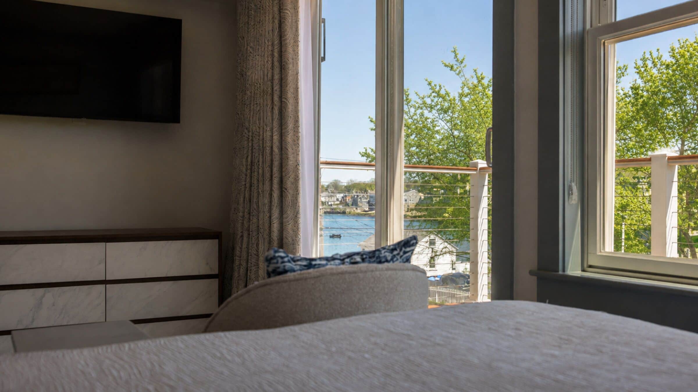 A bedroom with a bed, a TV mounted on the wall, and a view of a body of water and greenery outside.