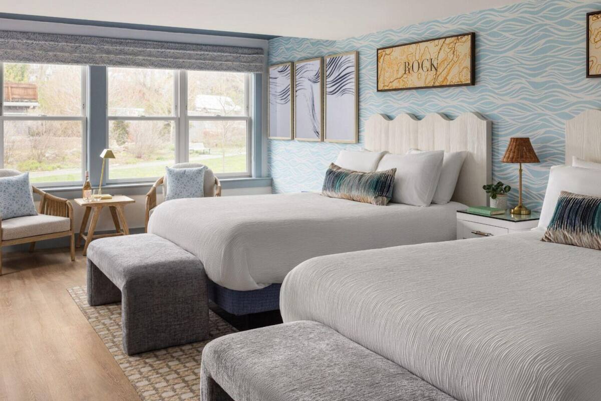 A hotel room with two beds, a window with a view, a small table, and a chair.
