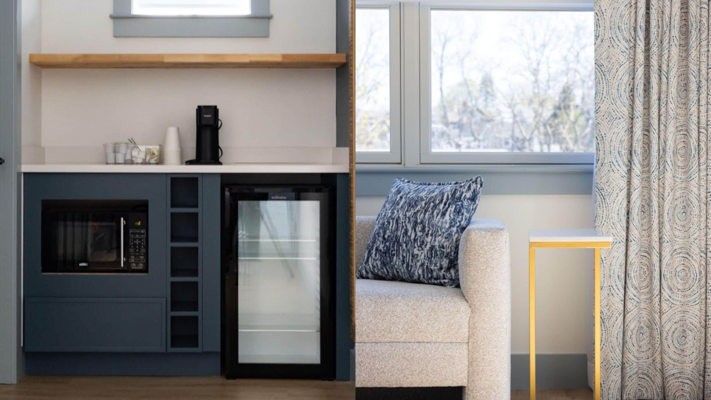 A compact kitchen with a microwave, coffee maker, and refrigerator. There is a sofa with a patterned pillow and a small table beside it.