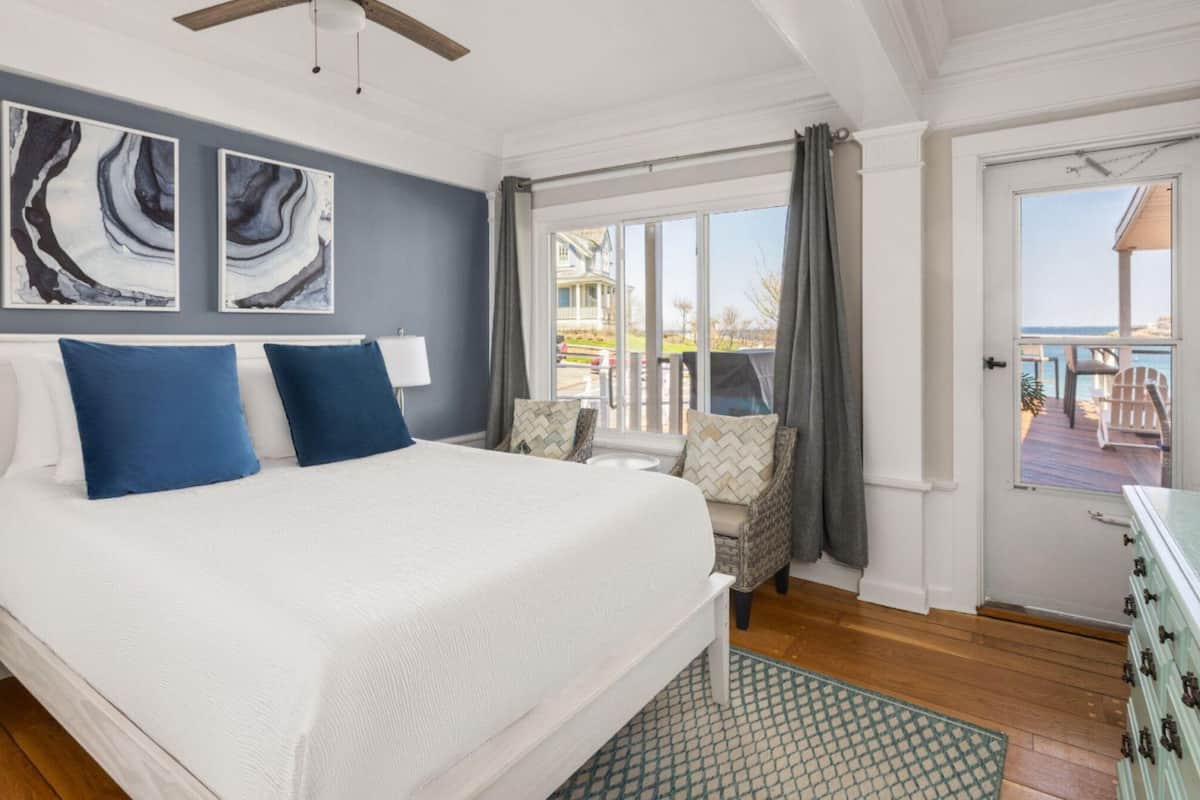 A bedroom with a large bed, a nightstand, a dresser, and a view of the outside.