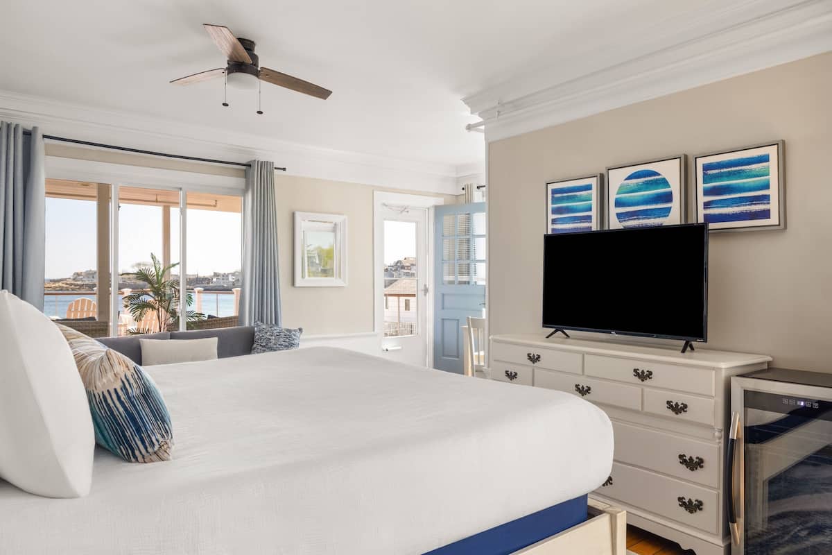 A bedroom with a large bed, a ceiling fan, a TV, and artwork on the wall.