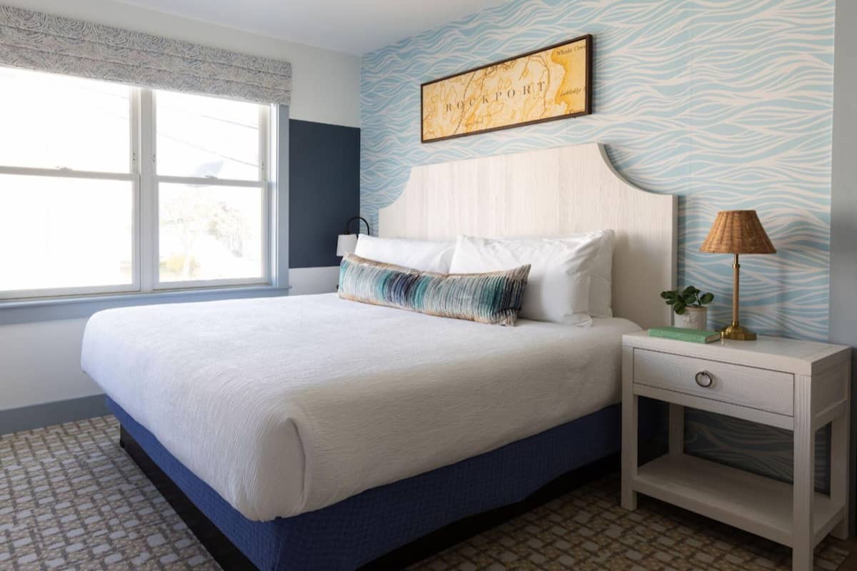 A bedroom with a bed, a nightstand, a lamp, a chair, a window, and a map on the wall.