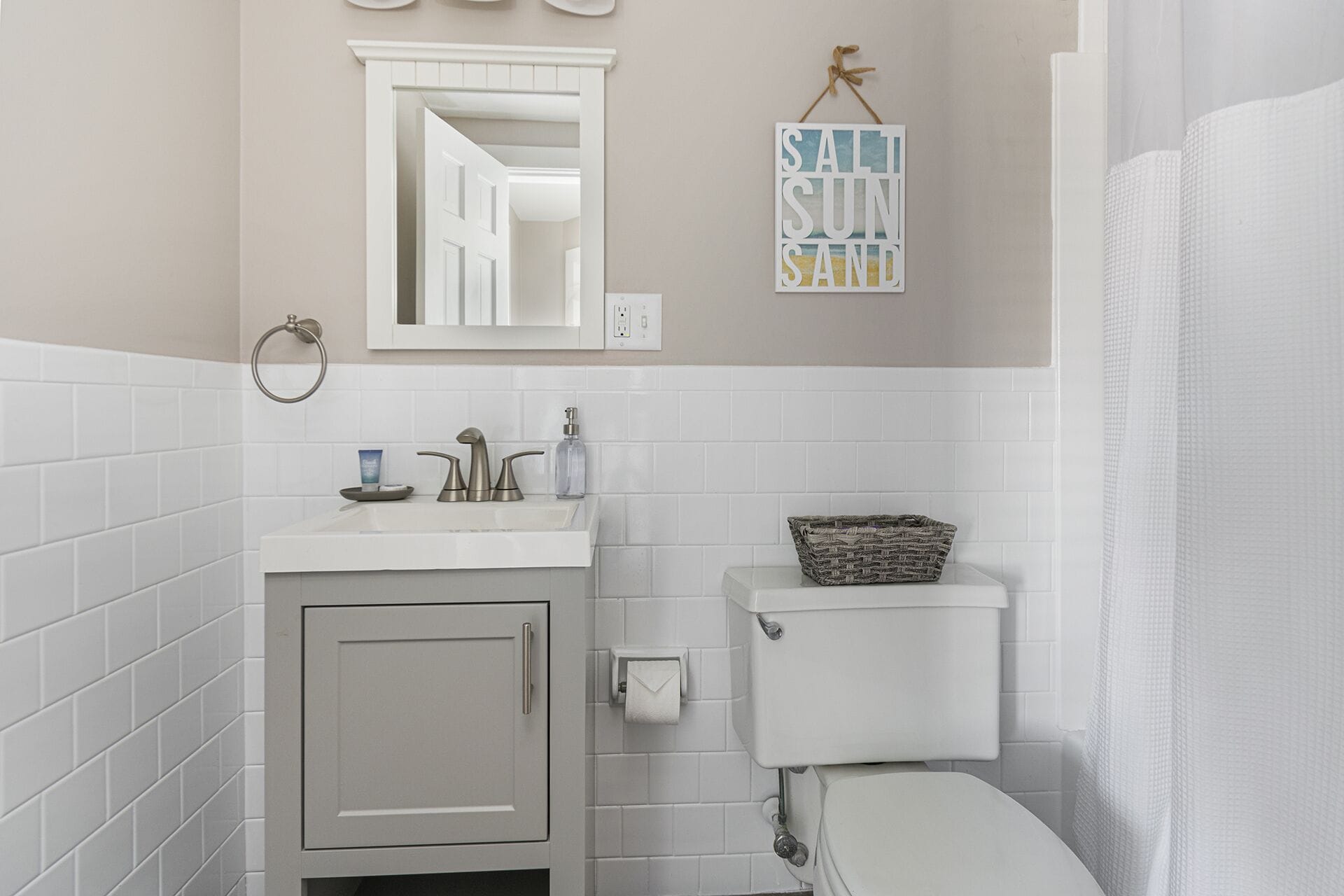A bathroom with white tiles, a sink with a soap dispenser, a toilet, and a towel rack.