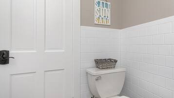 A bathroom with white tiled walls, a white toilet, and a basket on the toilet tank.