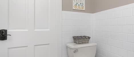 A bathroom with white tiled walls, a white toilet, and a basket on the toilet tank.