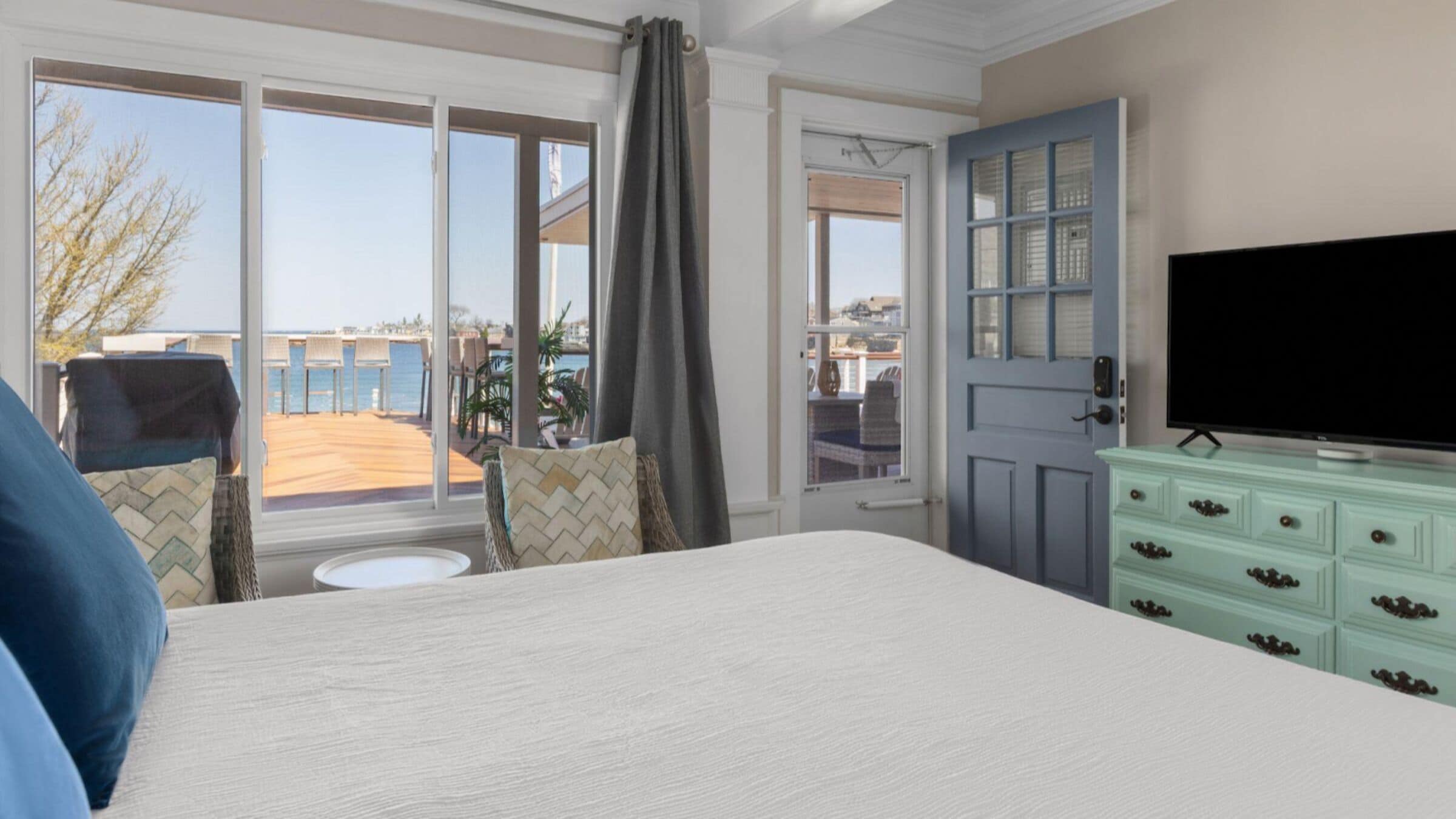 Une chambre d’hôtel avec un grand lit, une télévision, une commode et une vue sur la mer par les fenêtres.