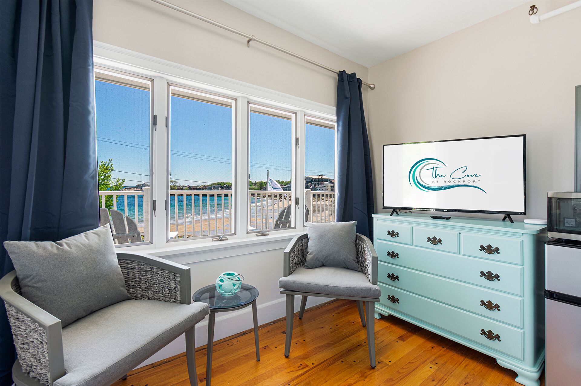 Habitación con vista al mar, un sofá, una silla, una mesita, un televisor y un aparador azul claro.