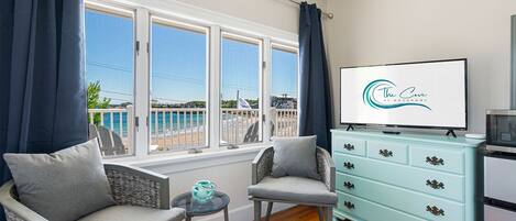 Habitación con vista al mar, un sofá, una silla, una mesita, un televisor y un aparador azul claro.