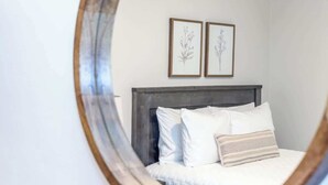 Un dormitorio con una cama, ropa de cama blanca, un cabecero oscuro e impresiónes botánicas enmarcadas en la pared.